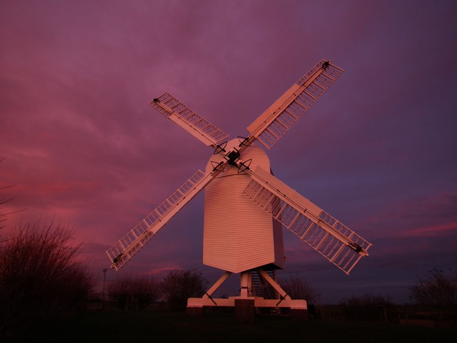 A white windmill against a pink and blue sunset
