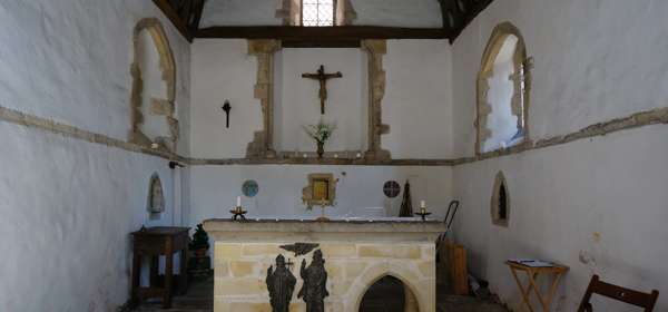 The interior of St Edmunds Chapel with a rough stone floor, whitewashed walls and a central stone alter.