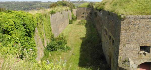 Exterior image of the Drop Redoubt fortress, brick walls and a green grass-lined dry moat. 