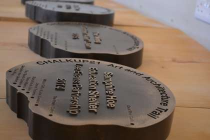A series of brown metallic raised plaques set into wood detailing stops on the CHALKUP21 Art and Architecture Trail 