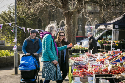 A group of people at a market stall full of fresh fruit and veg. 