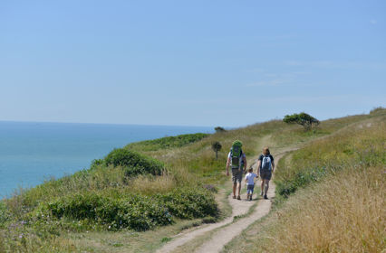 Two adults holding hands with a small child walking on the White Cliffs of Dover - blue sea and sky.