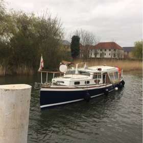 A wooden boat with a navy blue hull and white deck on the River Stour with reedbeds in the background.