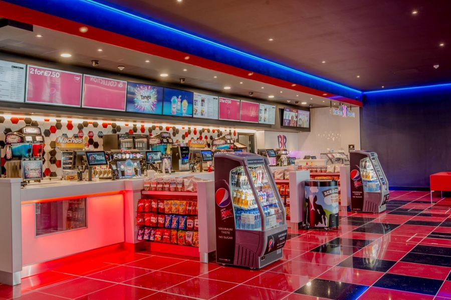 Interior of cinema reception with food and drink displays and shiny red-and-white tiled floor.