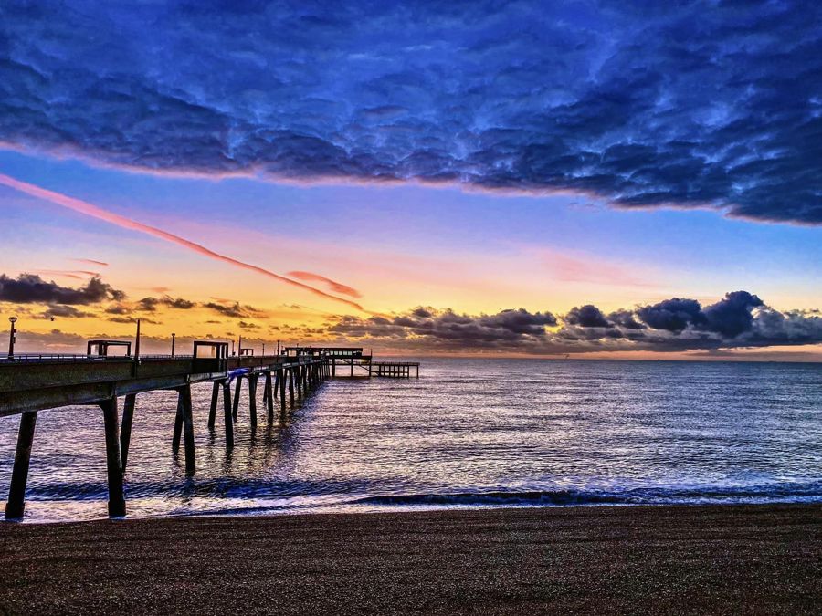 Deal Pier and beach, looking out to sea with a spectacular sunrise sky of yellows, pinks, blues and purples.