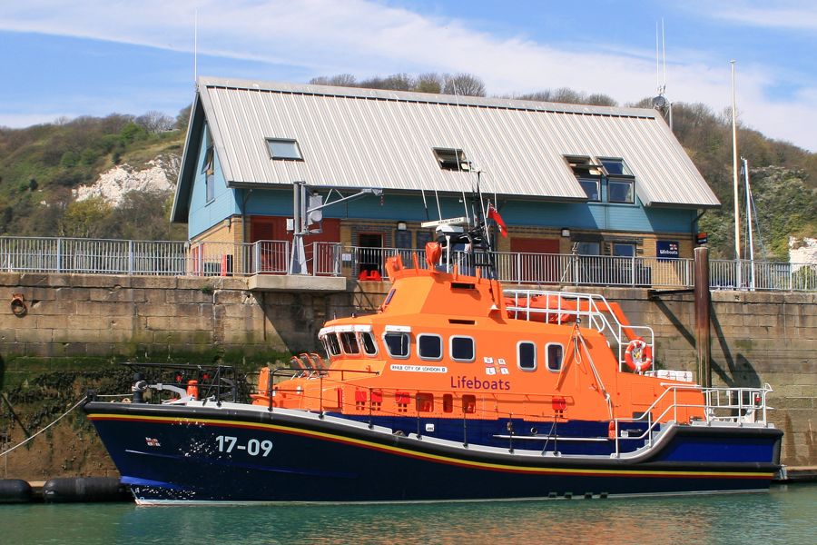 An orange and navy lifeboat in Dover Harbour in front of the Lifeboat station