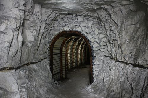 An arched tunnel entrance hewn out chalk and lined with corrugated metal and iron arches.