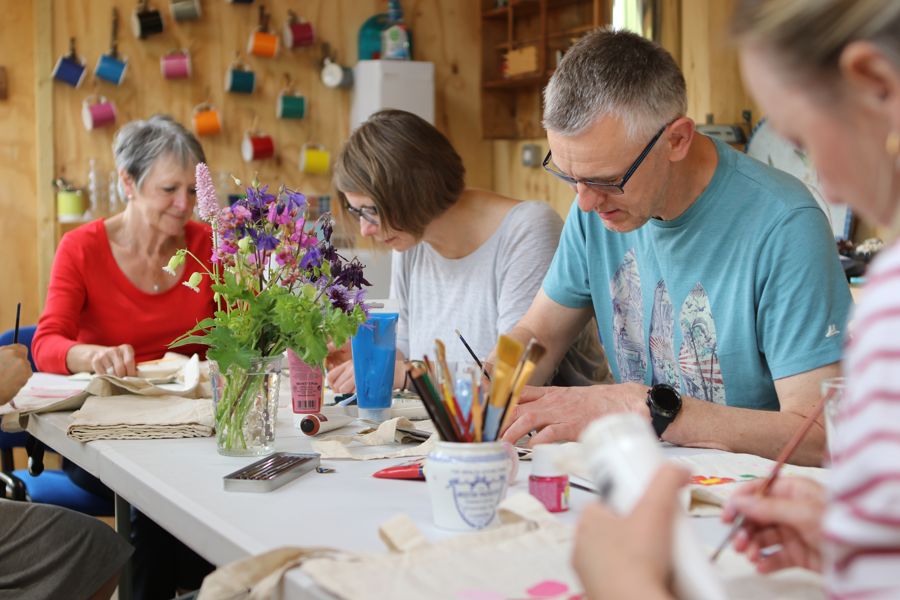 A group of people sitting round a table drawing. Pots of paintbrushes and flowers on the table.