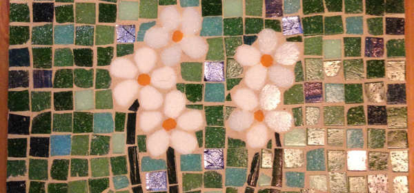 A mosaic tile made of green, white and blue pieces of ceramic forming the image of flowers.