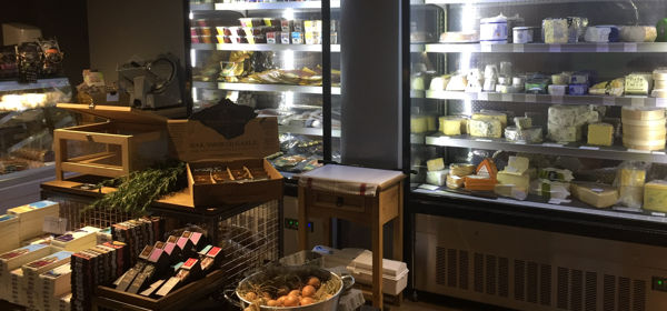 Interior of a delicatessen with fridge full of cheeses and a display of other foods.