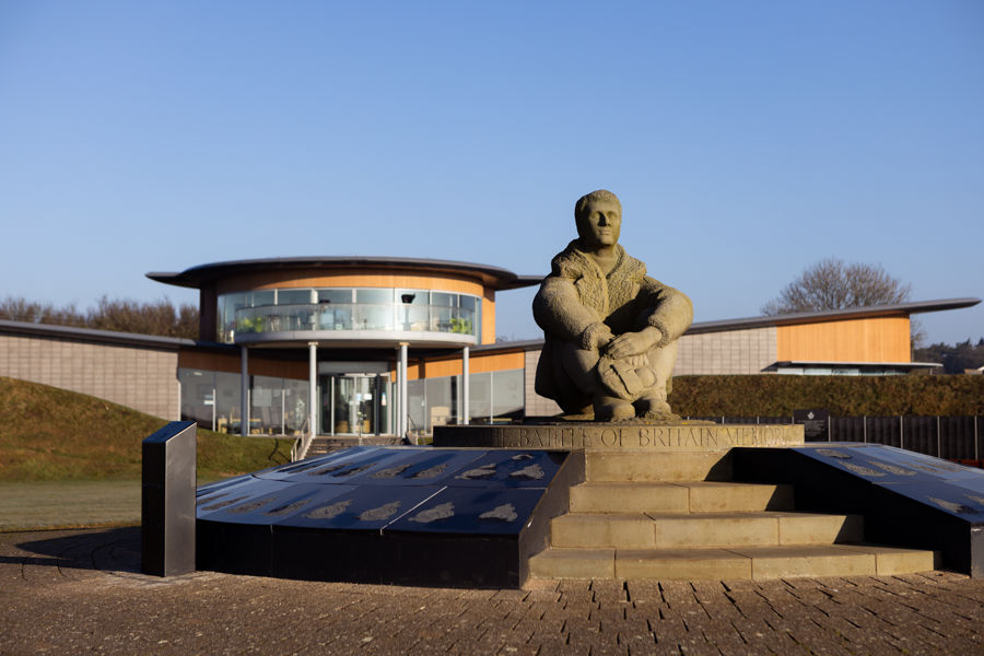 A granite statue of a wartime pilot to commemorate the Battle of Britain with the memorial centre behind.