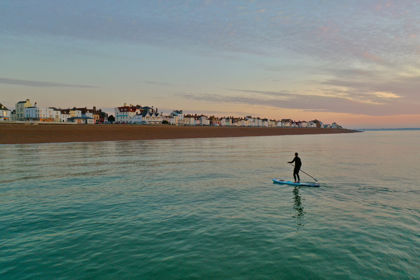 A person on a paddleboard on a calm sea with Deal seafront and beach in the background.