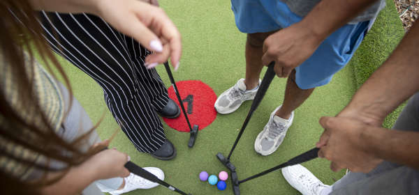 Looking down at four golf balls and clubs and four pairs of feet standing in a circle.