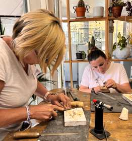 Two women at a work bench using hand tools to make jewellery.