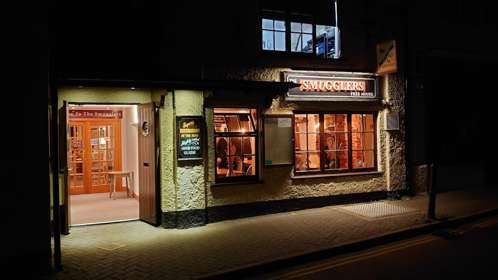 An exterior image of The Smugglers Inn at night with inviting lit doorway and windows