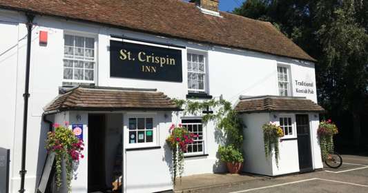 Exterior of the St Crispin Inn with whitewashed walls and colourful hanging baskets
