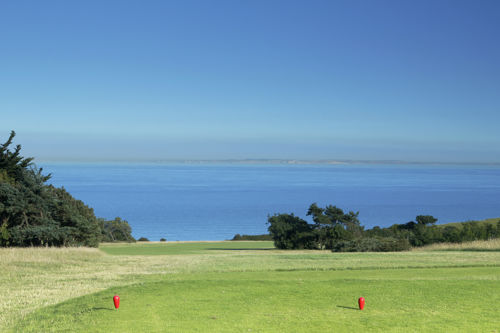A golf green with a blue sky and sea views in the distance.