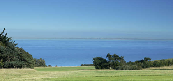 A golf green with a blue sky and sea views in the distance.
