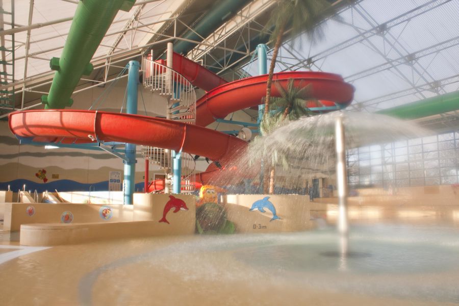Indoor pool at Tides Leisure Centre with curly red slide and water fountains.