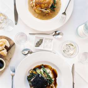 A meal for two laid on a white table cloth viewed from above. 