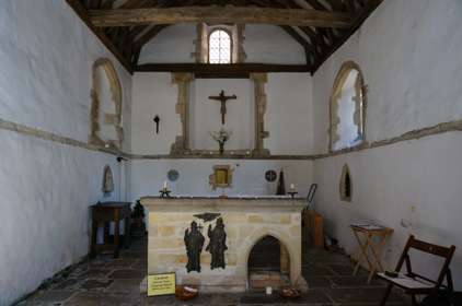 The interior of St Edmunds Chapel with a rough stone floor, whitewashed walls and a central stone alter.