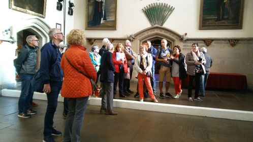 A group of visitors standing in a large historic hall listening to a tour guide.