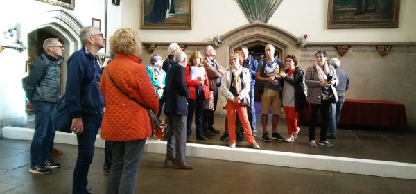 A group of visitors standing in a large historic hall listening to a tour guide.