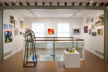 A gallery space with colourful paintings on the wall and sculptures on plinths