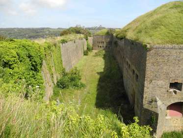 Exterior image of the Drop Redoubt fortress, brick walls and a green grass-lined dry moat. 