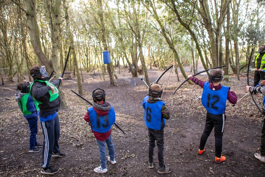 A group of children learning archery in a wooded area