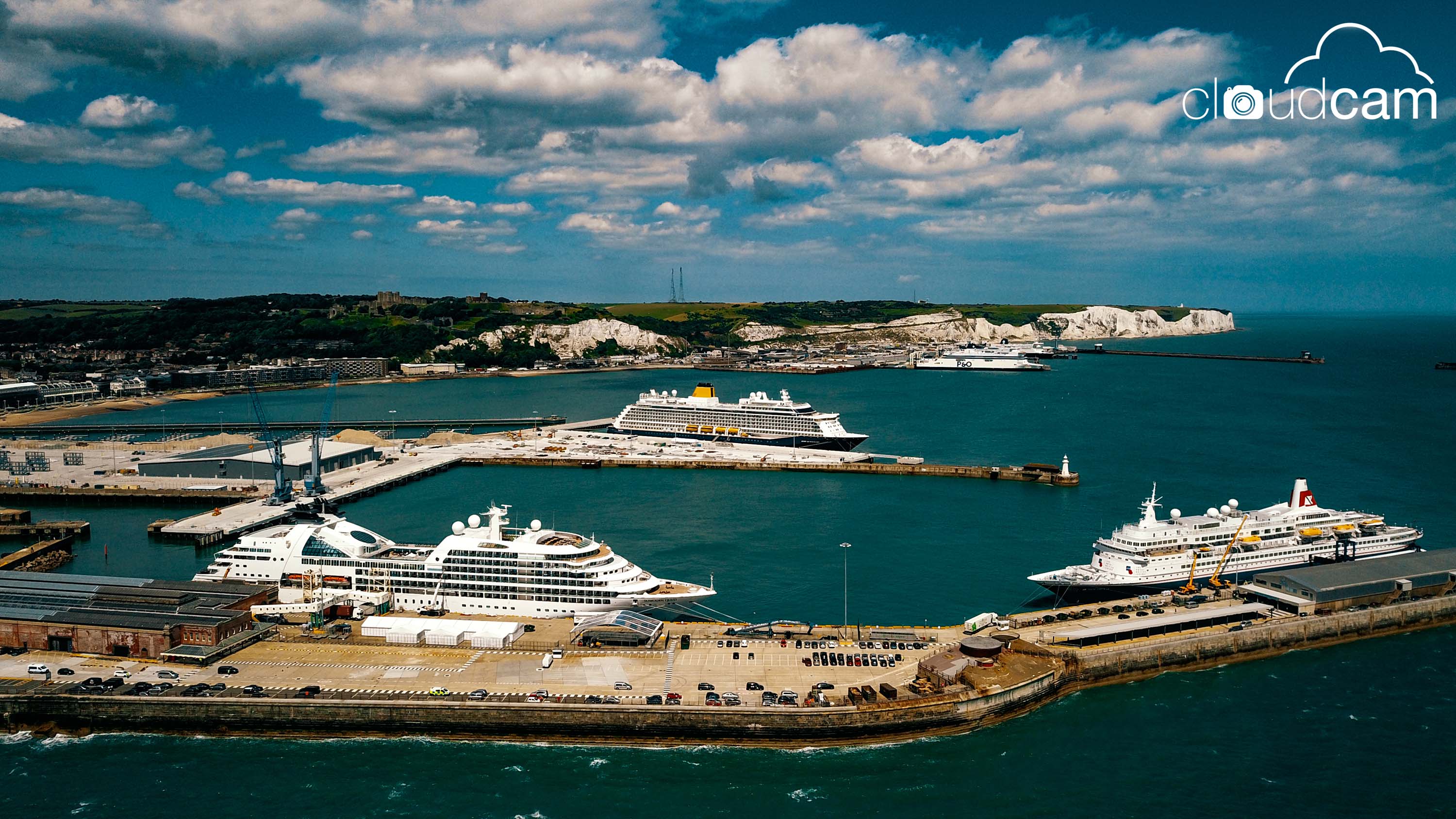 An aerial view of the Port of Dover with three cruise ships docked and the White Cliffs in the distance.