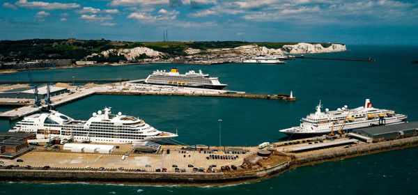 An aerial view of the Port of Dover with three cruise ships docked and the White Cliffs in the distance.