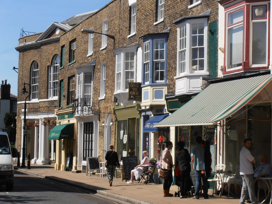 A street of Georgian buildings with shop fronts, a green-and-white striped awning in the foreground. 