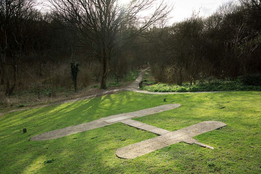 Paving shaped like an aeroplane in a grassed bank surrounded by trees.