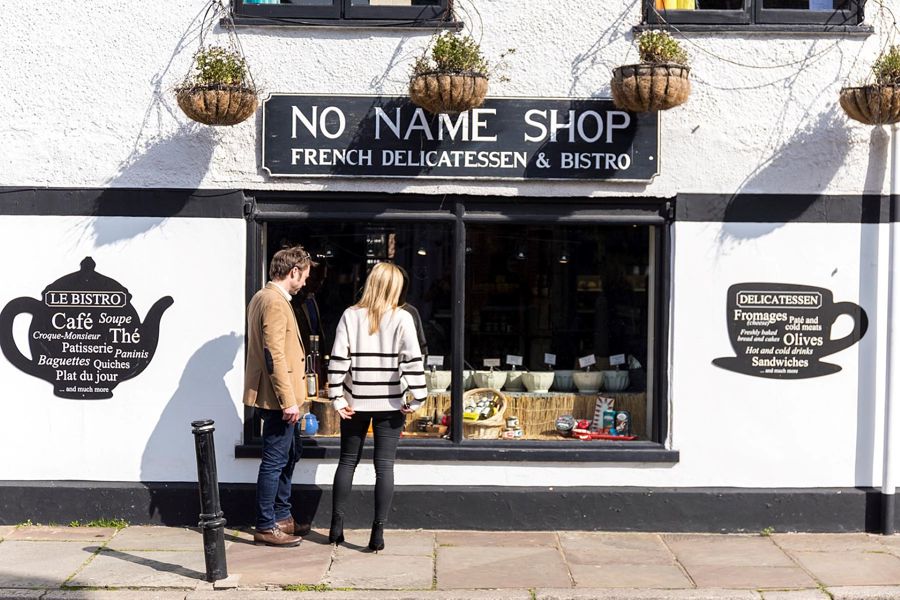 The exterior of the No Name Shop French delicatessen and bistro in Sandwich with a couple looking in the window displaying bowls of olives.