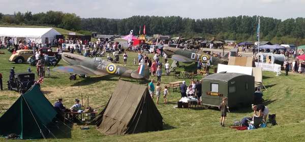A World War II re-enactment event with static spitfire planes, tents and people in military costume