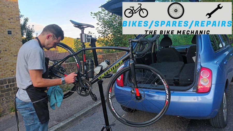A man repairing a bike on a street next to a blue car.