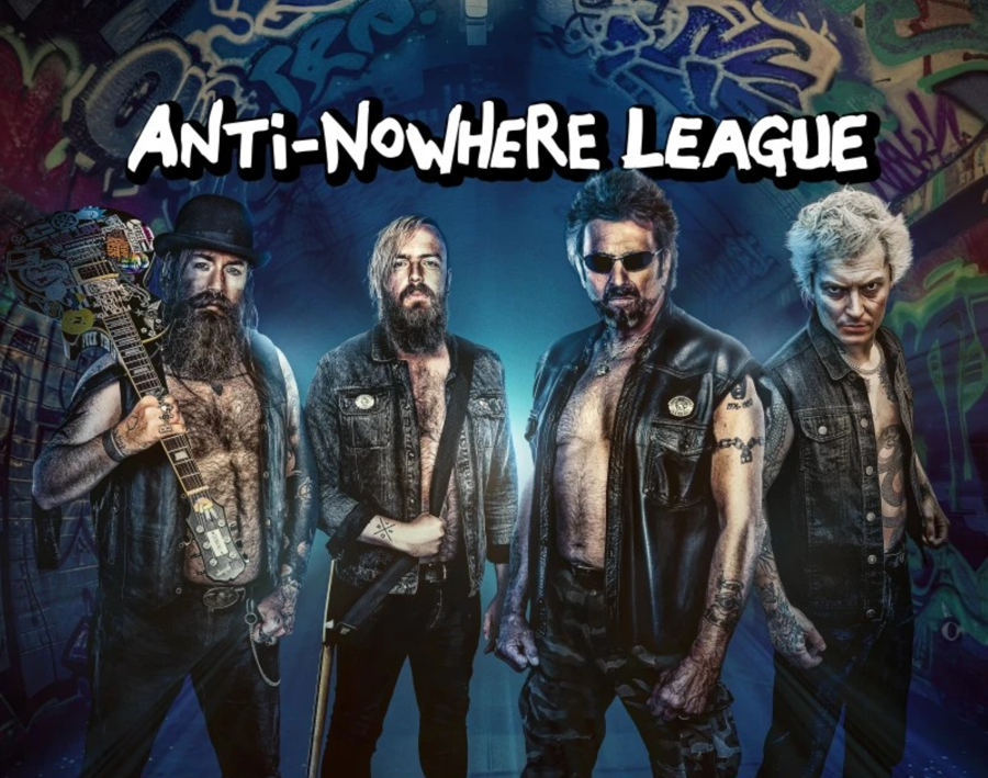 4 men wearing leather jackets with the front open revealing bare chests. 1 has a guitar over his shoulder.