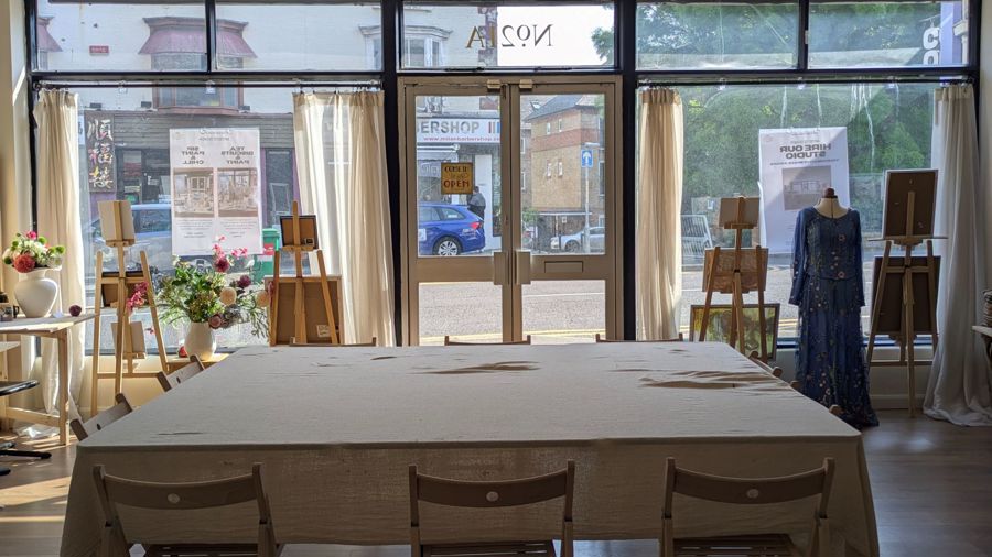 The inside of a shop with a large table covered with a cloth and easels in the window.