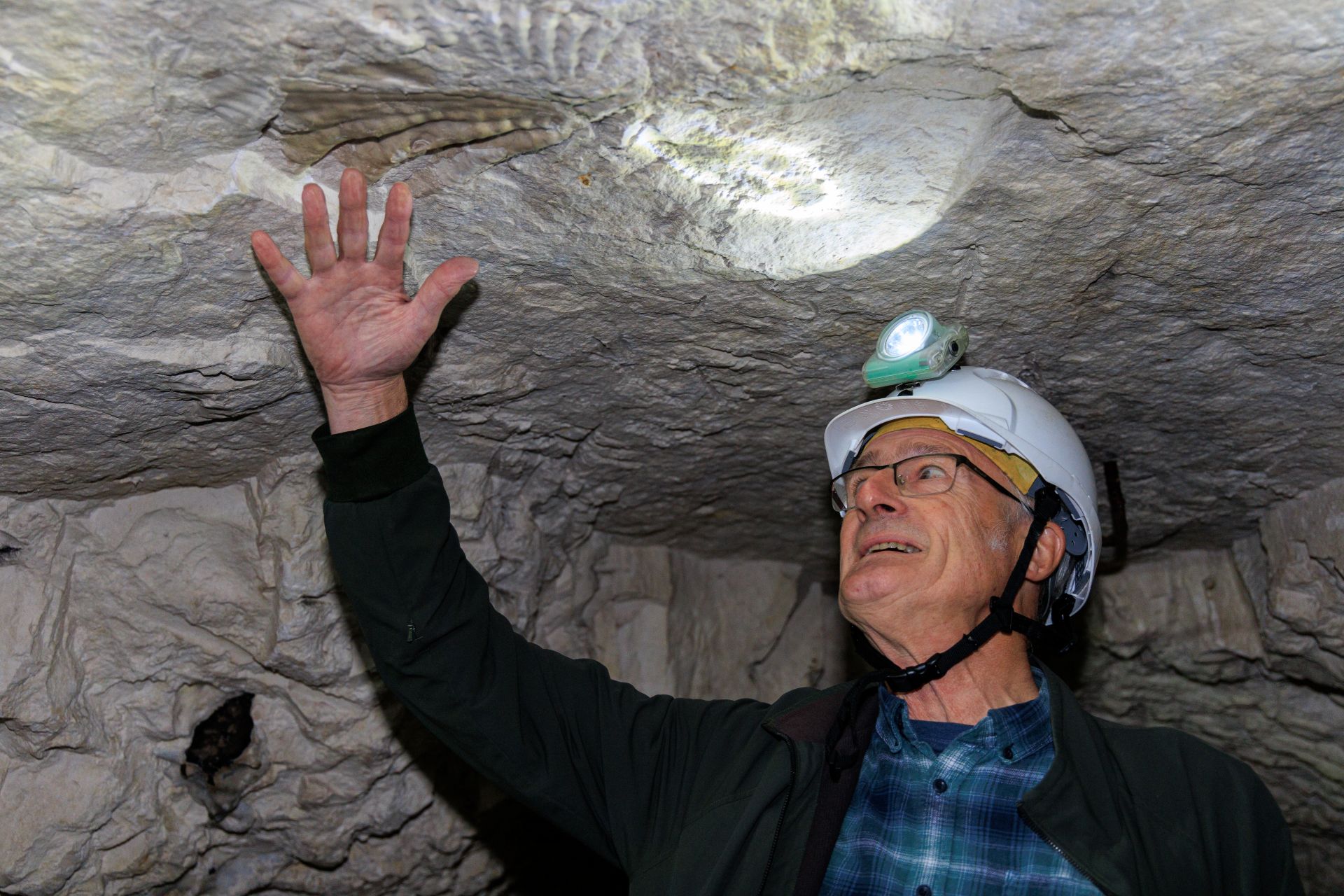 A man wearing a hard hat and head lamp in an underground chalk tunnel.