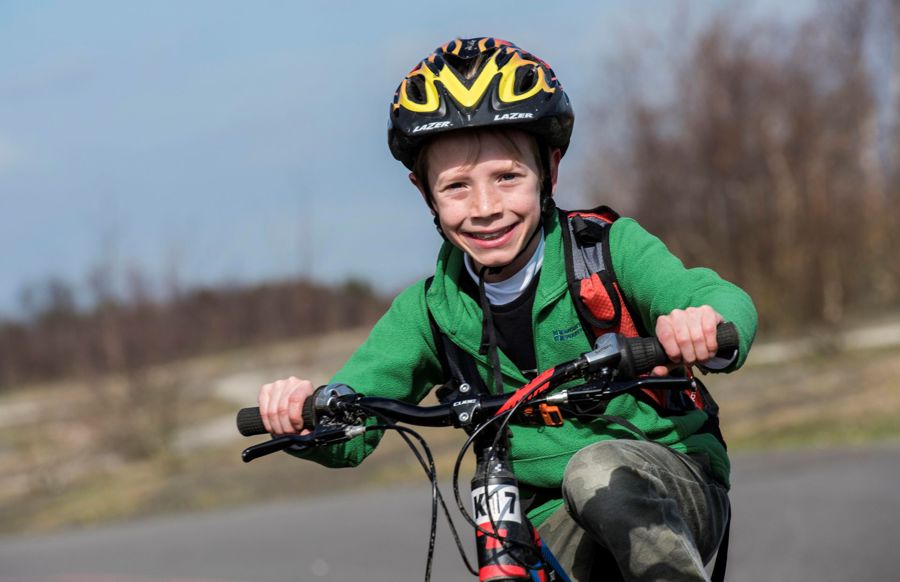 A smiling boy in a bike helmet and green top on a bike