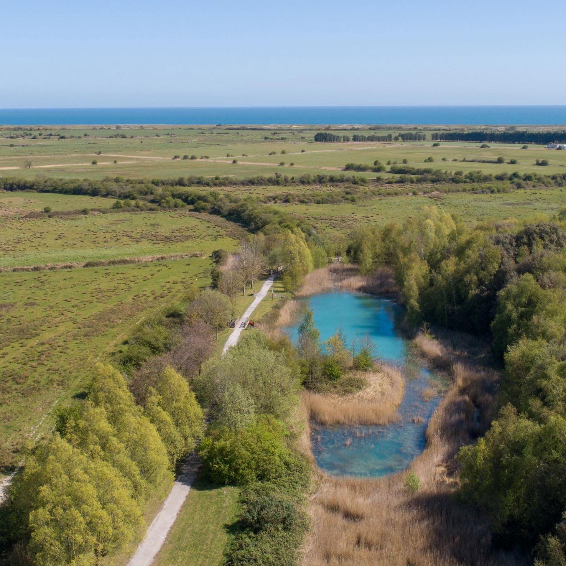 Blue lake surrounded by trees with sea in the distance