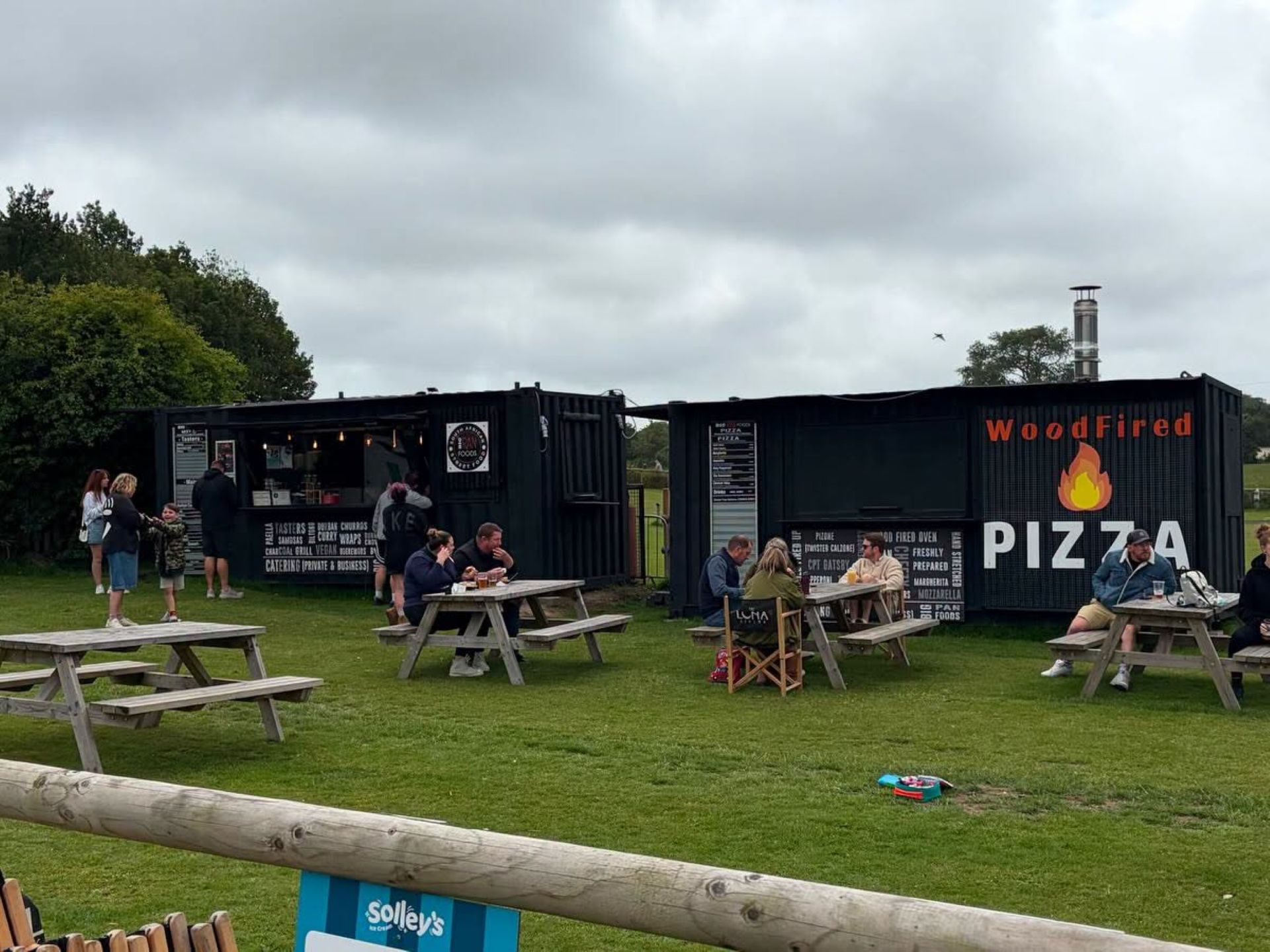 Two black converted containers with people at picnic tables in front 