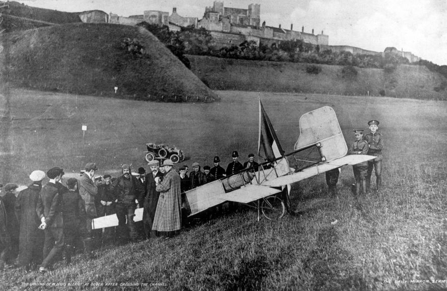 A group of men in early 1900s dress surrounding the first plane to cross the English Channel.