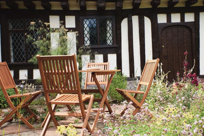 A black and white Tudor building with wooden garden furniture in the front garden.