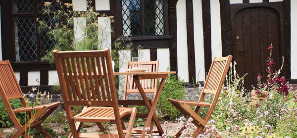 A black and white Tudor building with wooden garden furniture in the front garden.