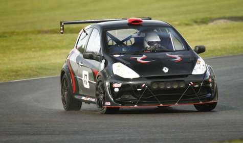Photo of a black car driven by a racing driver going round a race track.