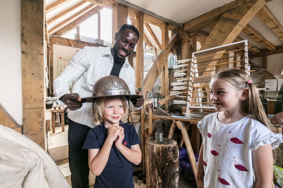 A man putting a metal helmet on a boy's head with a girl watching.
