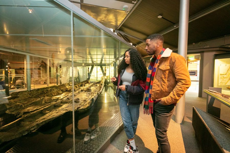 A man and a woman looking at a display case housing the wooden remains of the Bronze Age Boat.