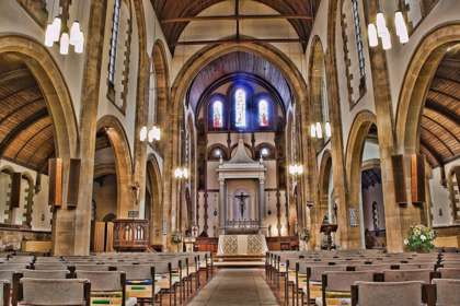 The interior of a large church looking up the aisle towards the alter and stained glass window
